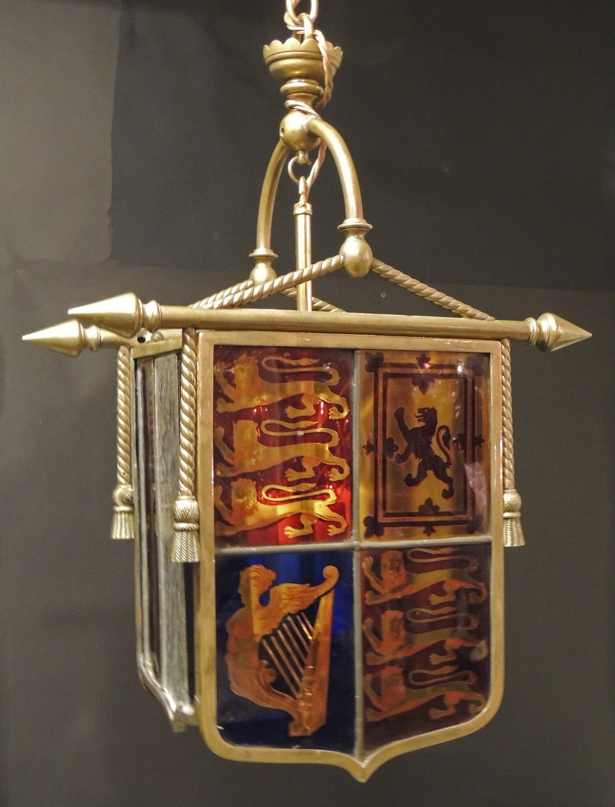 This four sided chandelier features the British coat of arms on one side and the Union Jack on the other all done in the shapes of banners and made of glass. In between the two banners there is a red white and blue panels. This chandelier is