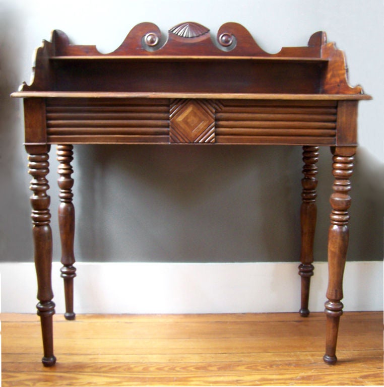 This British Colonial Jamaican sideboard was made in the early to mid-19th century and is made of mahogany. The decorative backsplash has a carved shell motif in its center, flanked by scrolls of West Indies origin. The body contains one drawer and