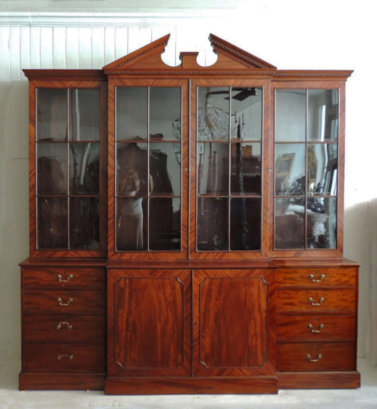 This mahogany breakfront was made in England around year 1770. The top section has four glass panels that contain shelves with adjustable height. Each of these panels are the same width. The bottom section has eight drawers on the outside with two