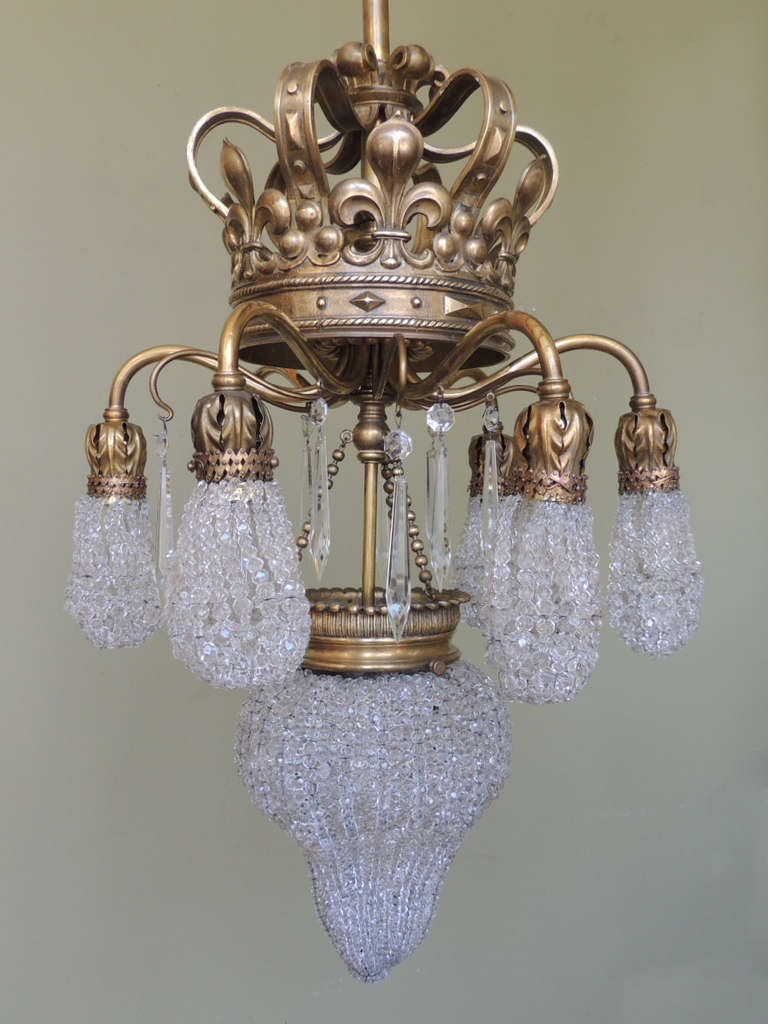This French chandelier was made in the early-20th century, circa 1900. The base of this chandelier is bronze and has crystal beading that surrounds both the small exterior and large central light. The top of the chandelier is in the shape of a