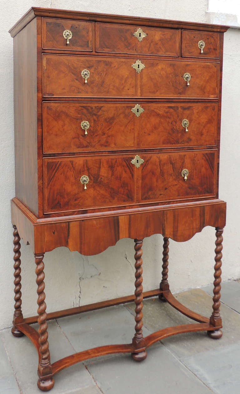 A beautiful English walnut chest on stand from the late 17th century. This piece features a lovely decorative skirt, beautiful wood, and antique brasses. The stand has unique spiral carvings, round feet, and bowed stretchers. Wonderful color and