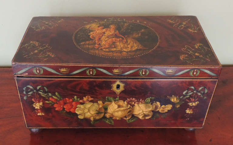 This tea caddy was made around year 1770 in England. This particular piece is hand painted and includes roses and other floral decoration on the lower front side of the item. The top features an oval painting of two angelic children with an adult