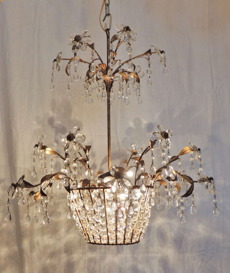 This chandelier was made in France during the mid-20th century. The body of this piece is made of tole and gilt and is covered with crystals of different shapes and sizes. The most prominent of these are arranged to form crystal flowers. This basket
