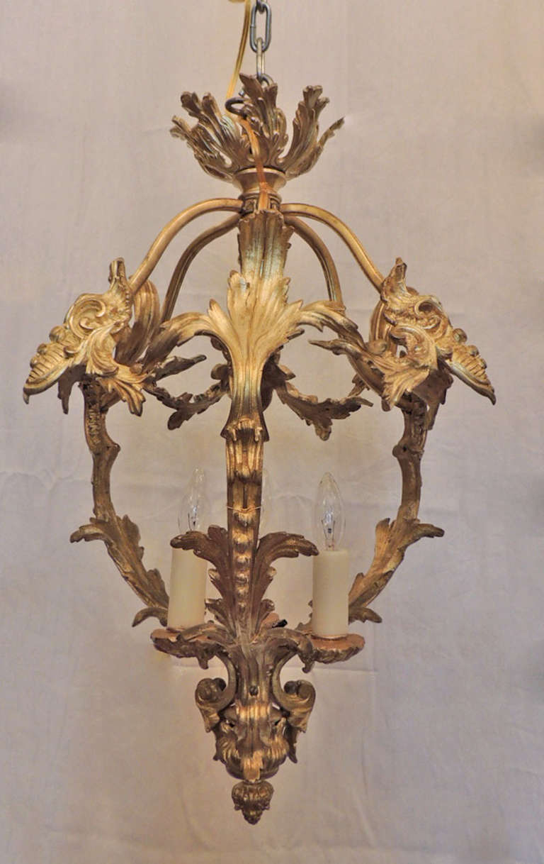 This pair of chandeliers were made of solid bronze, each containing three lights. The open bodies of the chandeliers are formed by intricate scrolling foliage. The bobeches beneath each of the three lights are shaped like scallop shells. The scallop