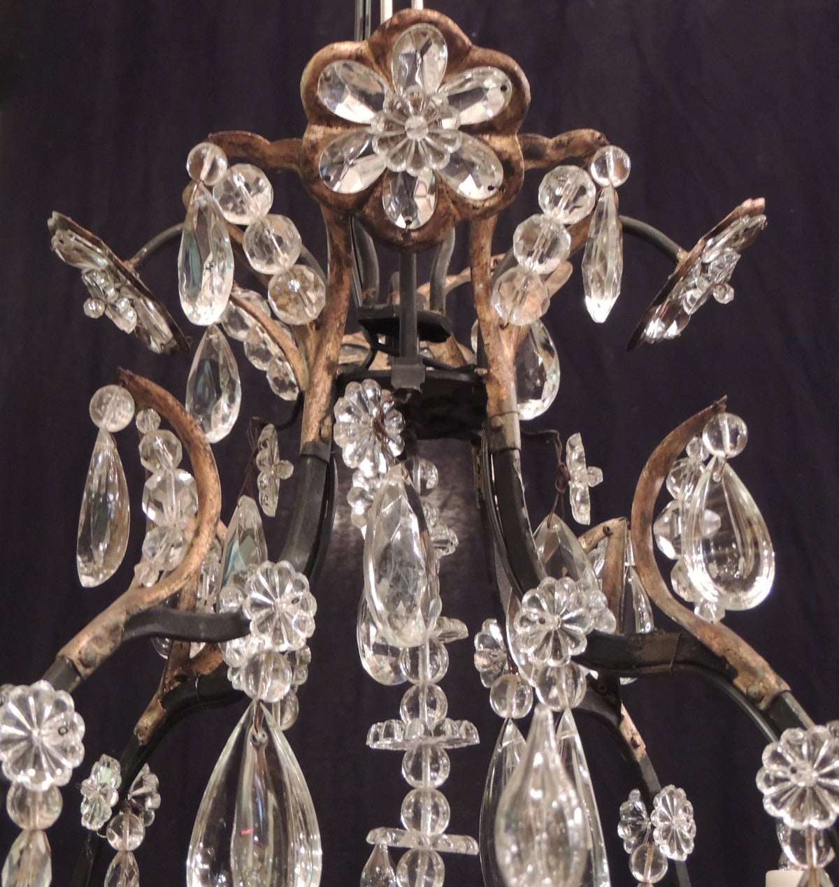 This chandelier was made in France during the first half of the 20th Century, circa 1930. This chandelier has an iron and tole frame covered in varied shapes and sizes of crystal prisms. The apex of the piece has crystal rosettes and beads. The