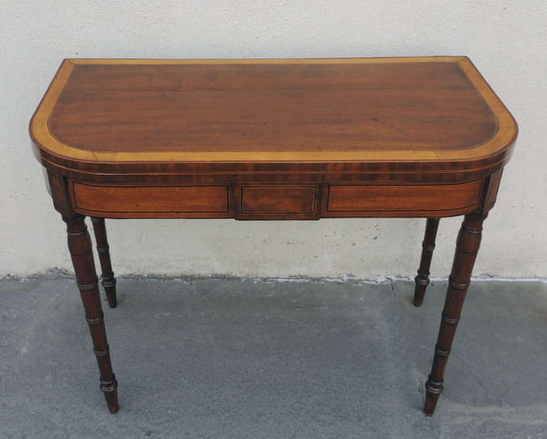 This card table was made in England during the first half of the 19th century. It was made of mahogany and features hand-turned legs. The two front legs of this piece each have an oval inlay detail and the unfolded top is covered in green felt.