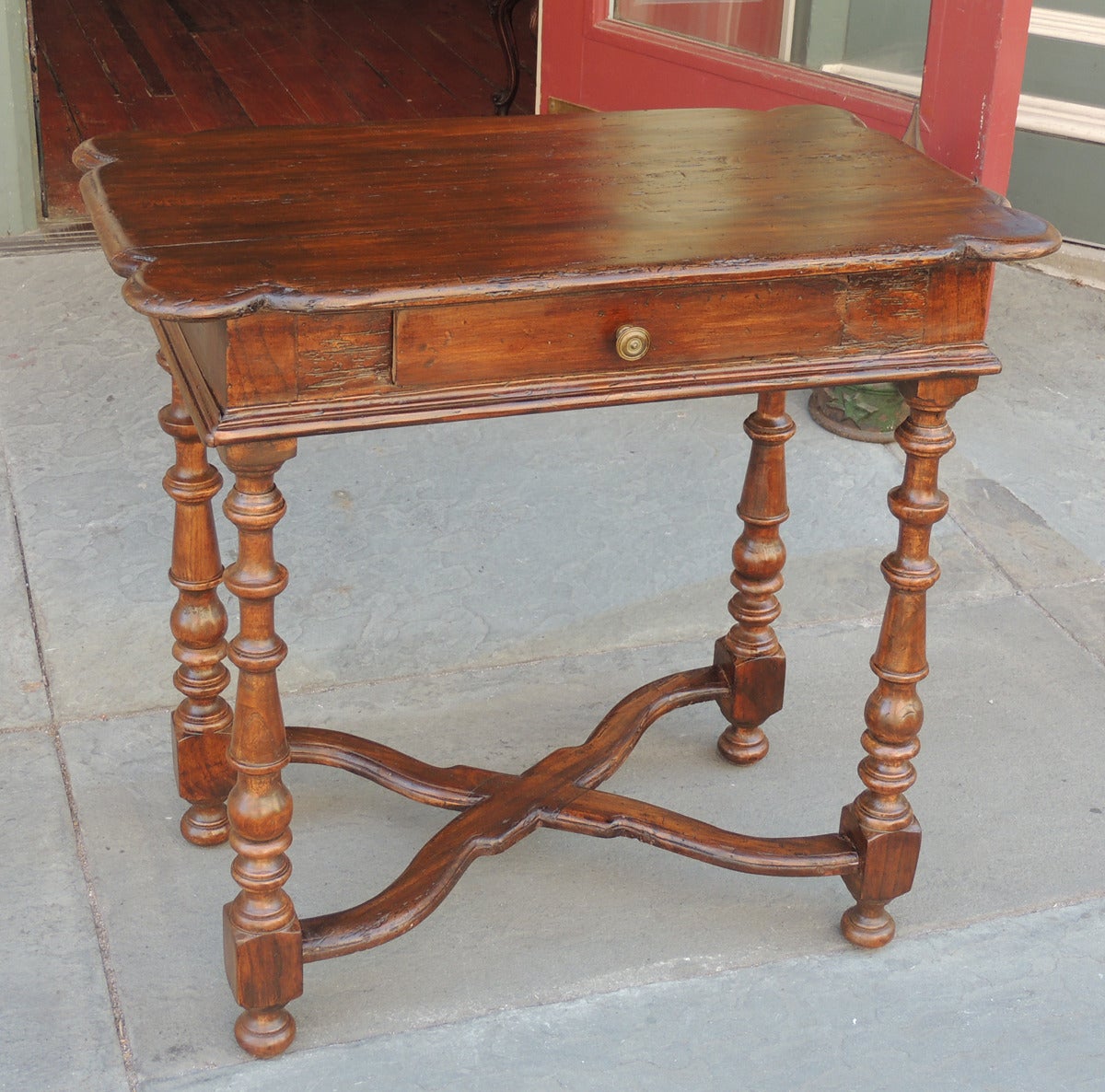 This table was made in Italy during the late 18th century and is constructed of pine. The table features a flat top with beveled borders and carved rounded corners above a single drawer. The table is supported by four hand-turned legs with