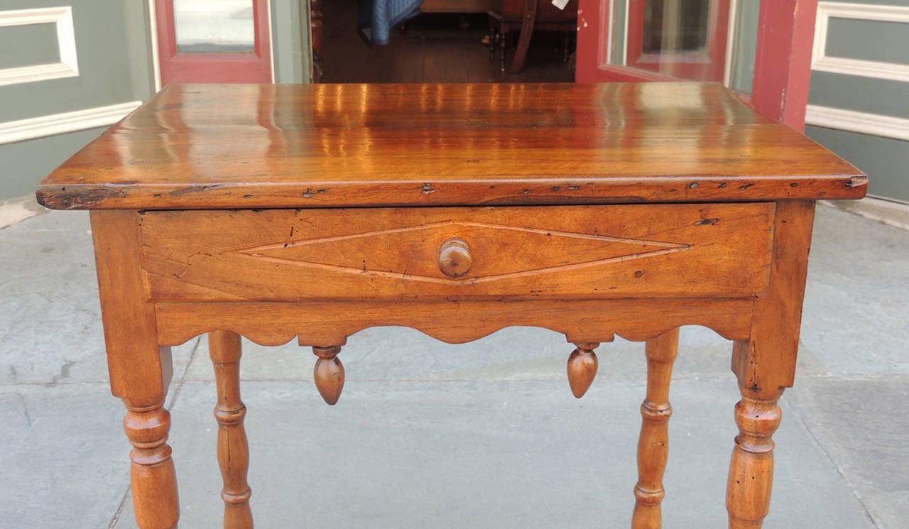 This table was made in France during the early-19th century and is made of pear wood. This table features a flat top with a square surface above a single drawer and carved skirt accented by acorn finials. The top section is supported by four