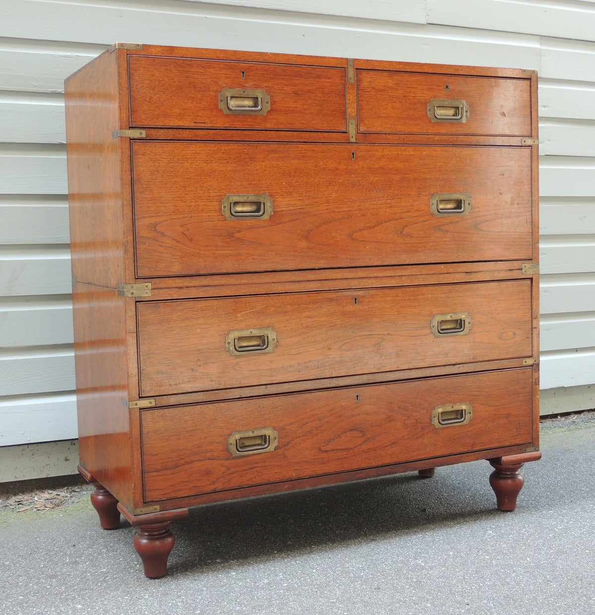 This English Campaign chest is made of teakwood and features five locking drawers. The detachable top half of the piece features two drawers above a large lower drawer. The lower half features two drawers that sit above four simple turned vase feet.