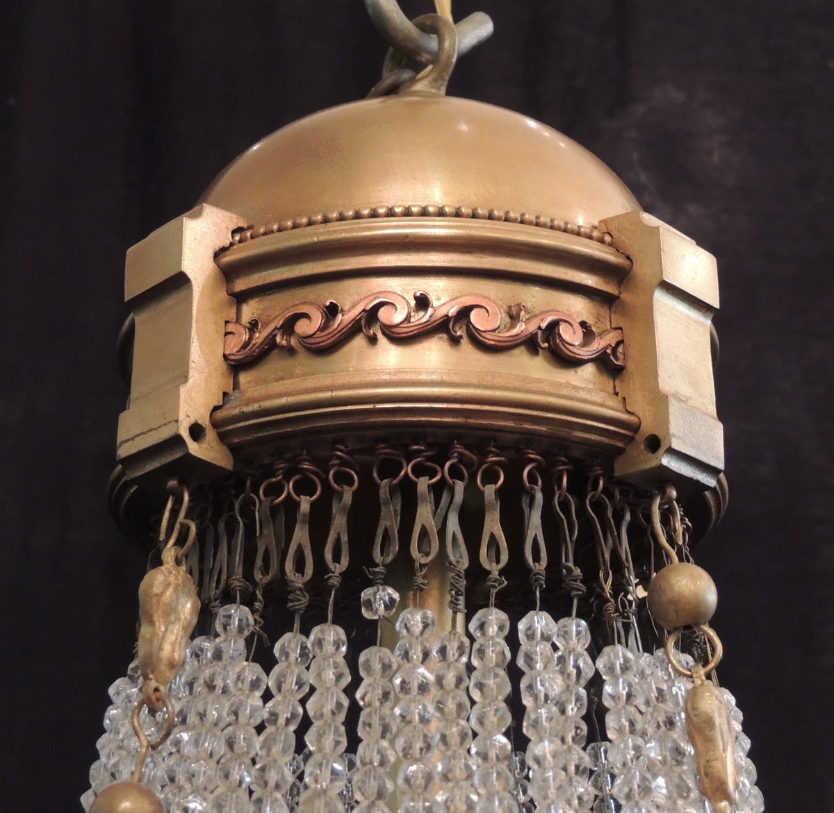 This chandelier was made in France during the first half of the 20th century, circa 1900. This empire style fixture has a bronze dome top with an S scroll border with many hanging fastened crystal chains and three bronze chains. The two types of