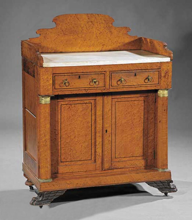 A classical birdseye maple washstand, circa 1830, with a shaped back splash and marble top. The body contains two drawers and two doors with Philadelphia turned rear fee and winged paw feet on the front.