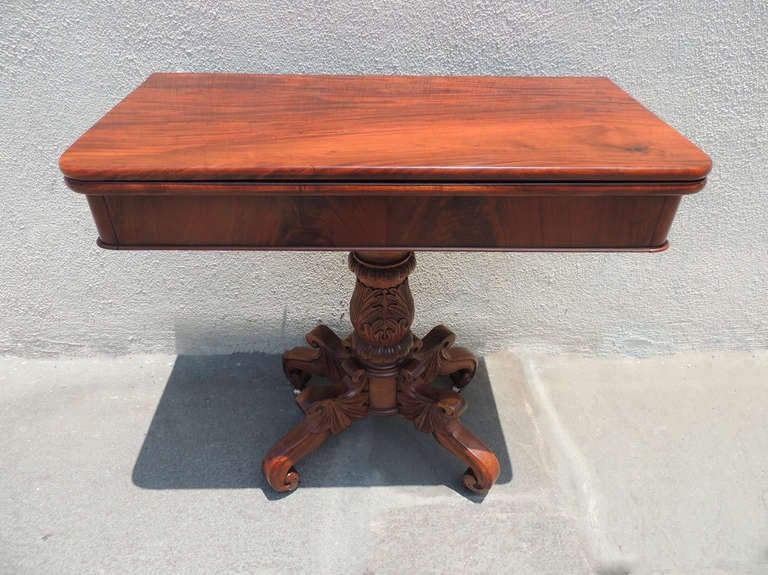 This Mahogany table has unique hand carved stand featuring vertical acanthus leaves going up along the middle. The legs of the stand are scrolled with with tropical flower motif. This piece was newly waxed and refinished.