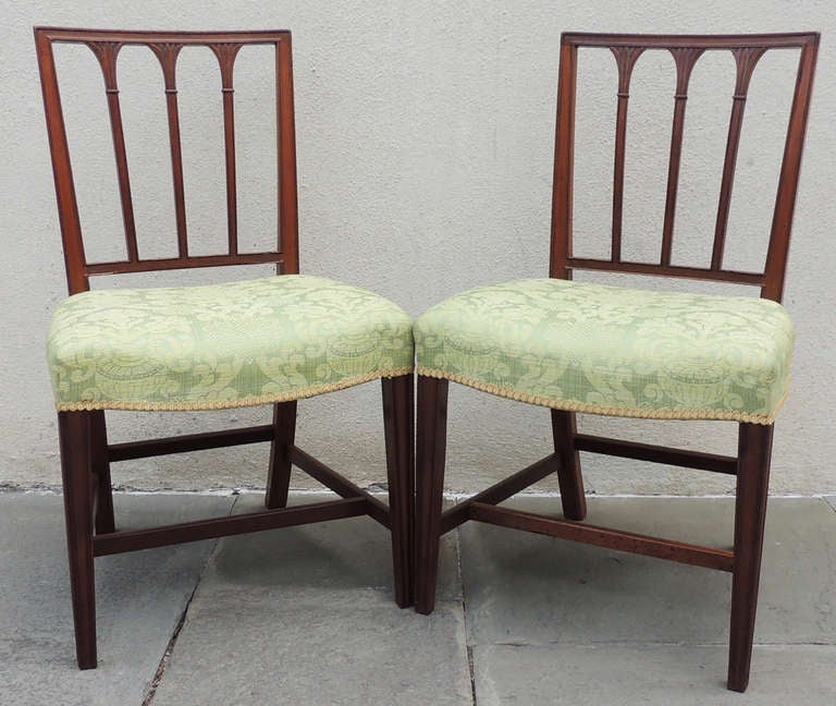 These English mahogany side chairs feature square backs and three thin spindles. The tops of the spindles have palm-leaf capitals. The recently-replaced green cushions are fastened with visible antique brass tacks that add character to the chairs. 