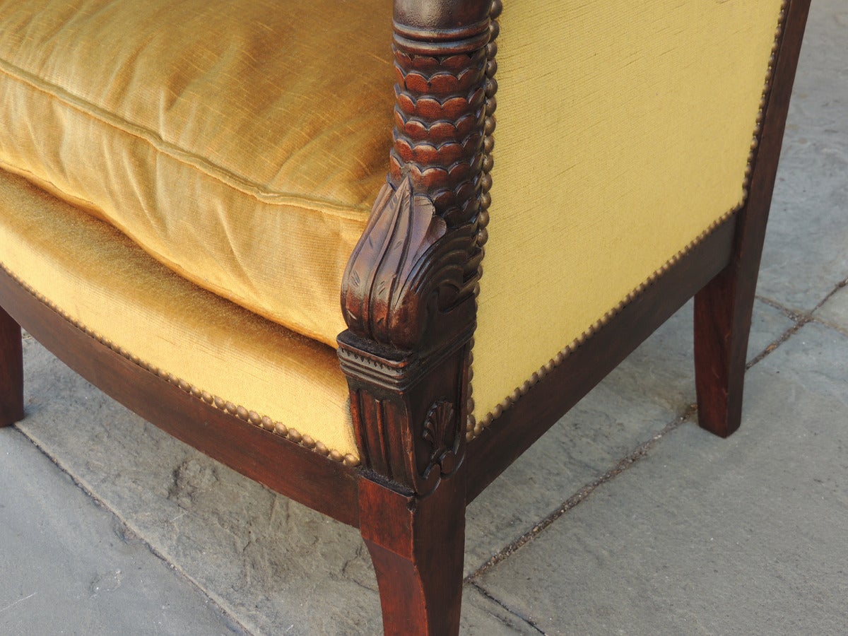 This pair of chairs is beautifully carved with square backs and velvet upholstered bodies. The arms feature dolphins with scale and leaf carvings at their junctions with the chair backs and seats. Small shells are carved into the sides of the arms