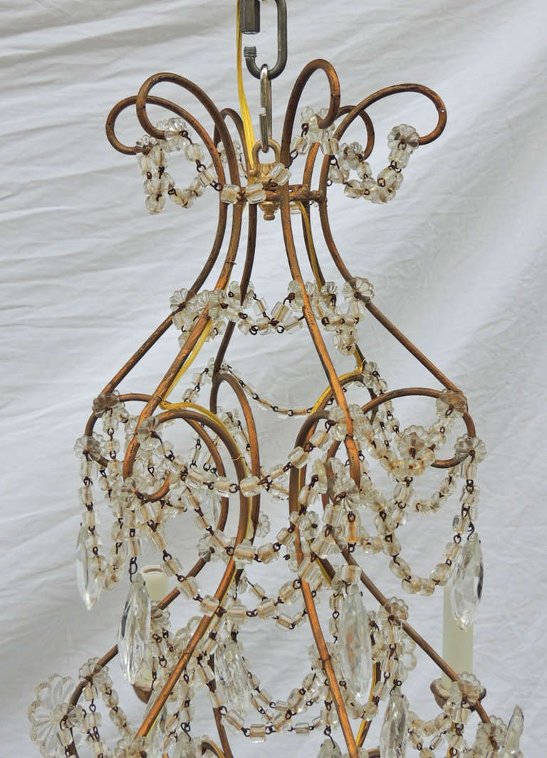 This chandelier has a gilt iron body with wooden bobeshes. The piece is decorated with crystal swags, tear drops, and rosettes. There are six thin gilt iron arms, each are French wired.