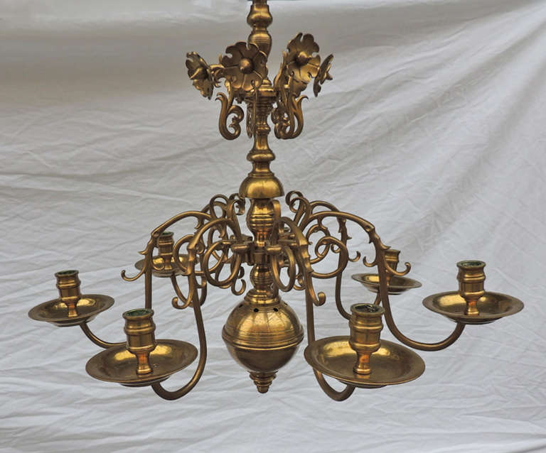 This small, rare chandelier has a hand-spun brass ball and stem and cast arms. Each of the seven arms are solid brass and feature scrolls of different sizes. This piece was originally made to hold candles but can be French wired to accommodate