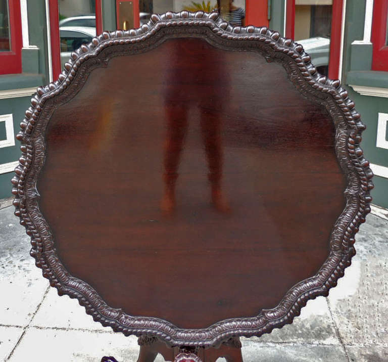 This mahogany tea table was made in Ireland in the 18th Century. It features carved lion feet, and hand carved baluster. The table top is in a scallop shape with an egg and dart outer border and braided inside borders. There is a original birdcage