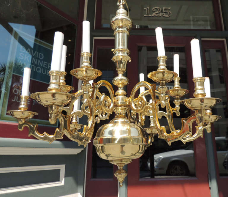 This chandelier was made in the United States during the first half of the 20th century. This chandelier features a central ball with a hanging finial. The body of this piece is a hand turned brass spindle structure with six curved arms. This piece