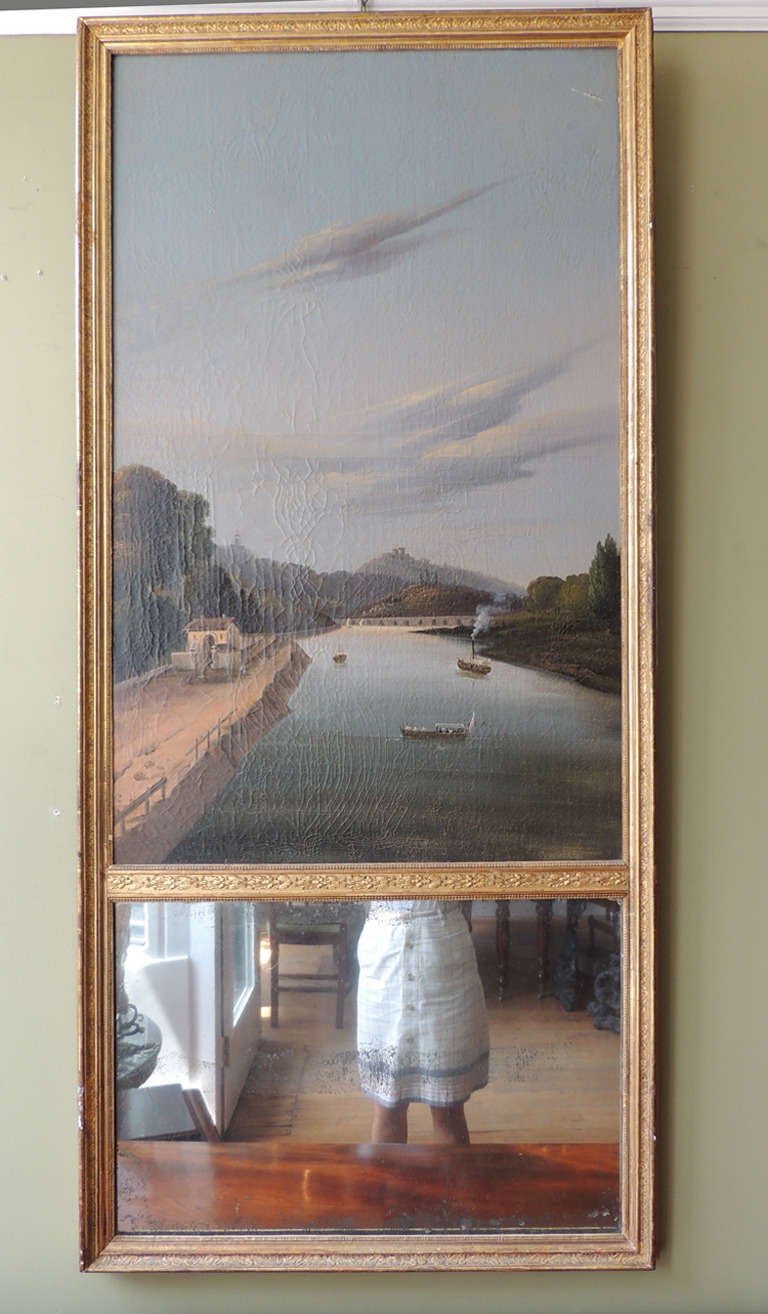 This French mirror dates from the 19th century, featuring hand-carved and gilded frame surrounds an oil on canvas painting of a river scene above the mirror. On the reverse side is an inscription which reads 