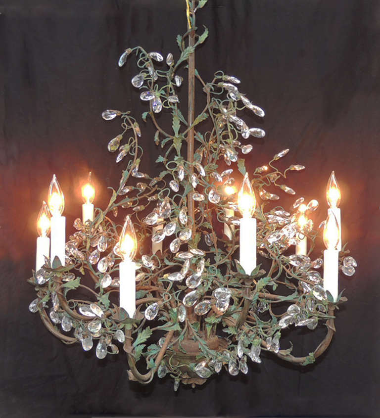 This chandelier was made in France in the early half of the 20th Century, circa 1900. The structure of this piece is iron and decorated with tole foliage and crystal leaves. The iron has a beautiful patina. The tole foliage is hand painted green to