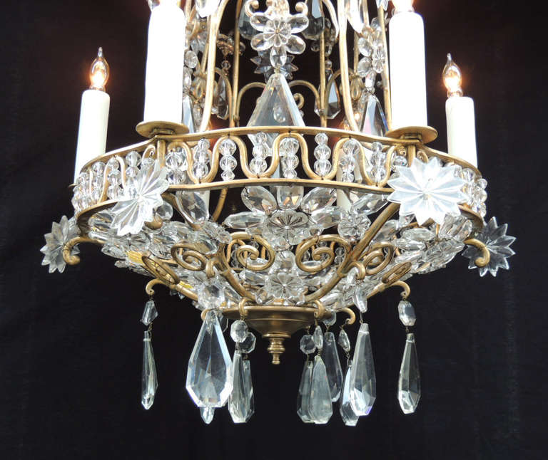 This chandelier was made in France during the early-20th century, circa 1910. This piece has a bronze base with a birdcage style frame. The bottom forms a bowl with crystal beads and rosettes. Teardrop crystal prisms hang from the base of this piece.
