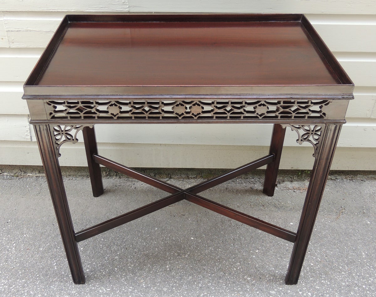 This English Chinese Chippendale mahogany tea table was made in the early-19th century. The table has a simple gallery above carved pierced fretwork with corner brackets. The base of the piece features Marlborough legs and a simple X-stretcher. This
