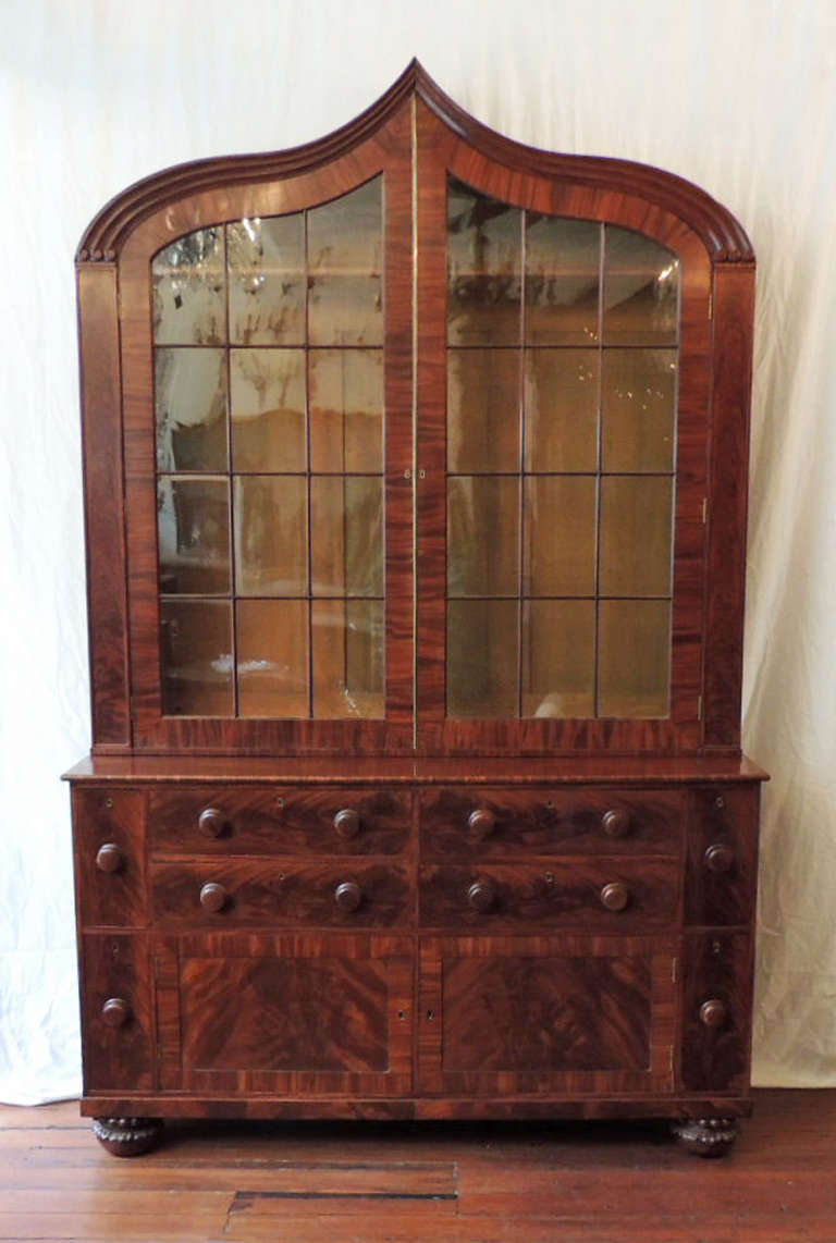 This bookcase was made in the early 19th Century, circa 1820.  This piece has a writing slide in the middle center drawer. This bookcase has wonderful round feet with foliage decoration. There are eight drawers and two cabinets. The top features a