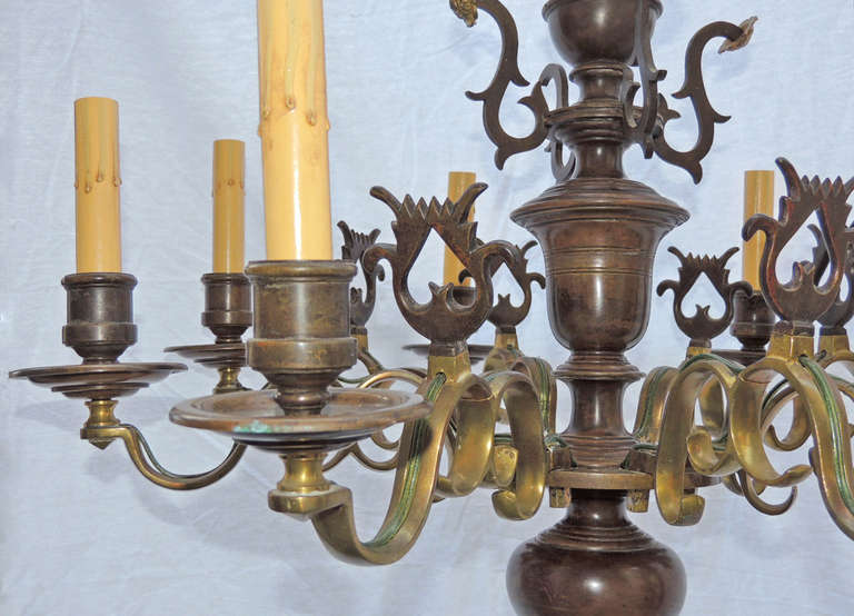 This chandelier was made in the early 18th century, possibly earlier. This piece is made of solid brass and features many unique design motifs. The arms are curved with simple scrolls topped with abstract lyres.  The base of the piece features a