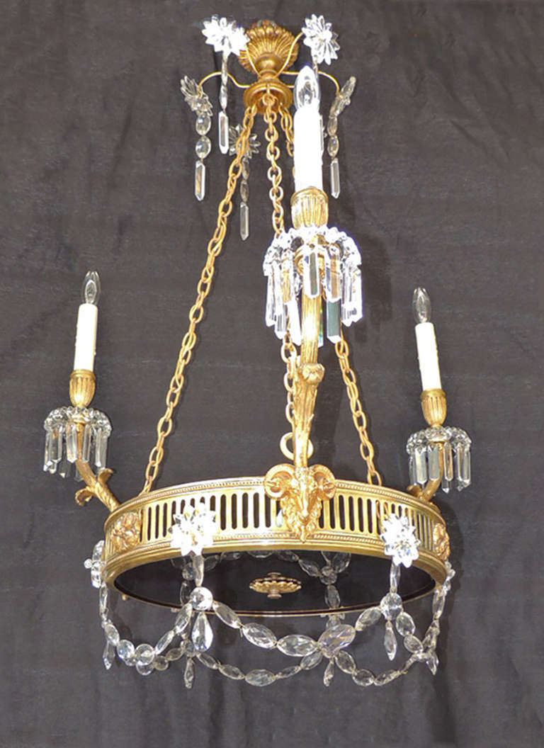 This chandelier was made in France in a Russian style and is made of brass and bronze with a deep violet glass bottom and a central brass flower detail. The side of this piece features three rams heads, flowers, and star-shaped crystals anchoring
