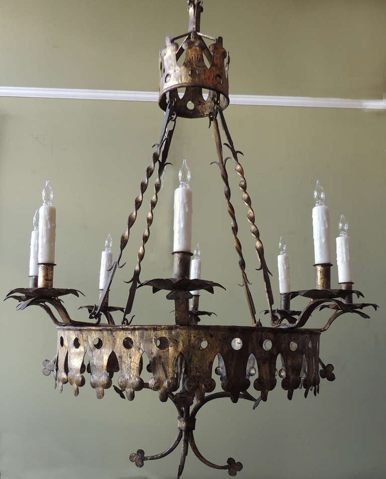 This chandelier was made in the 1920s in Barcelona, Spain, and is made entirely of iron and gilt. This piece features Gothic designs around the border of the base with a crown top.