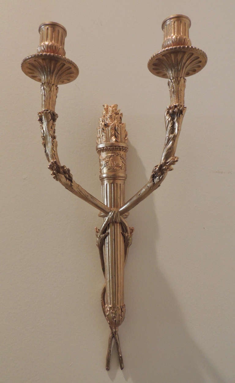 These four sconces are made of solid Doré bronze. The bodies of these sconces feature a cast central quiver and two crossed arms. This set has beautiful and rare casting. The sconces originally held candles, but have been wired to accommodate