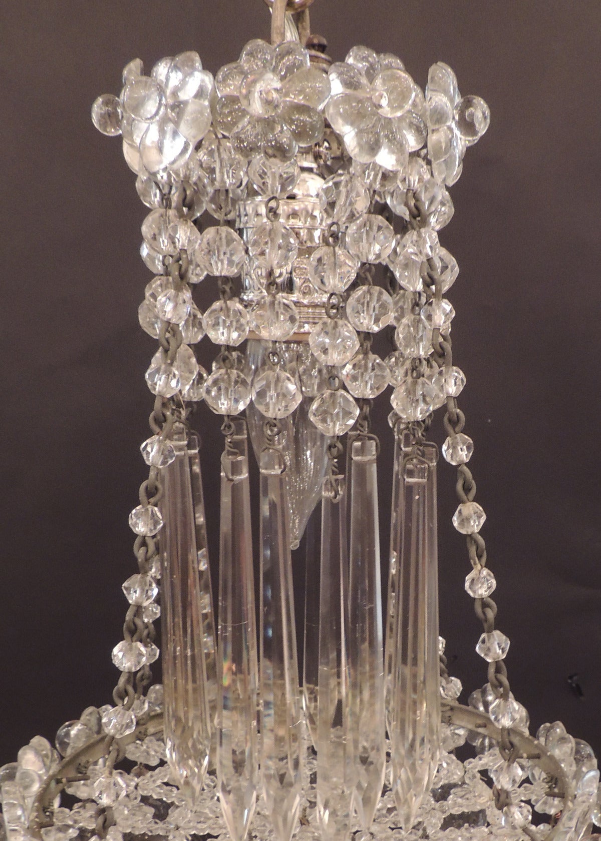 This chandelier was made in the early-20th century, circa 1900. This piece features crystal rosettes at the top with hanging prisms covering the body of the piece. The base of the chandelier is a waterfall shape with Venetian crystal balls. The