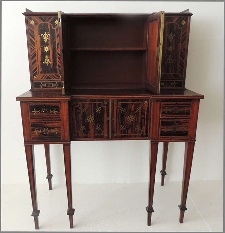 This desk was constructed in the first half of the 19th century and is made of coromandel with brass inlay. The upper part is divided into four sections that feature vertical star and leaf-type brass designs. The middle top section is divided into