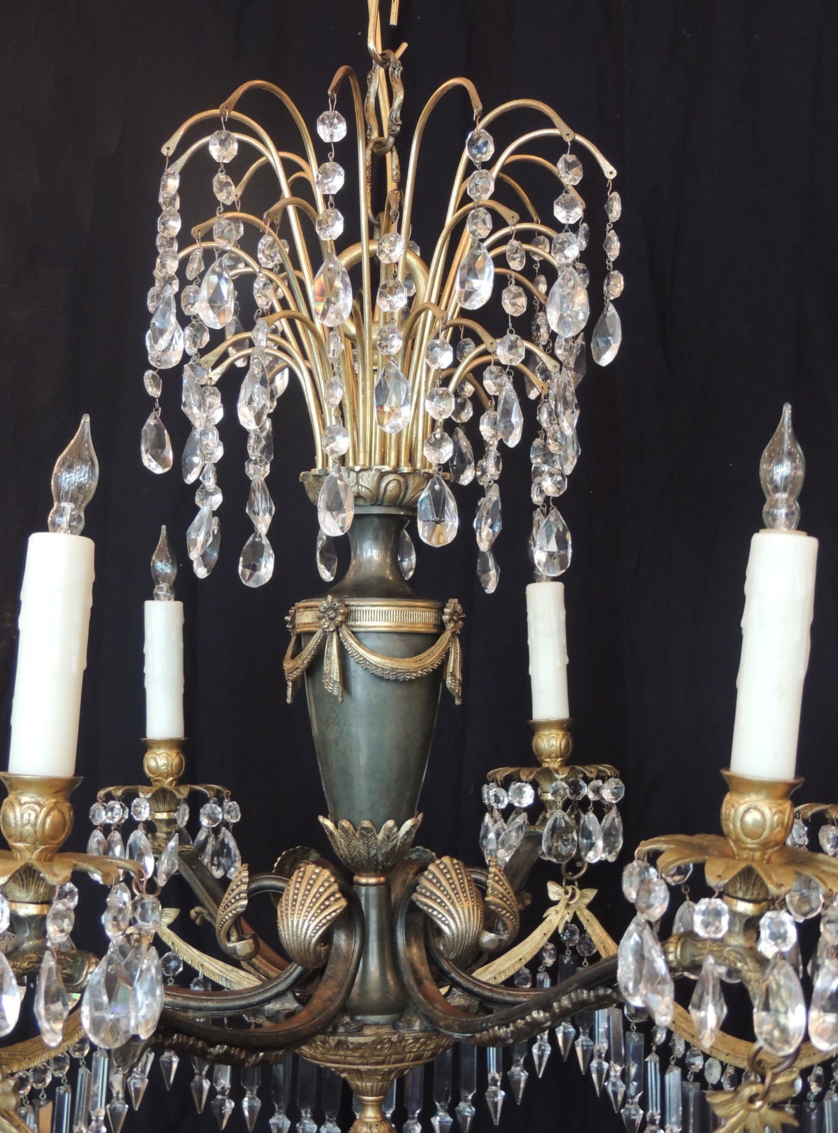 This chandelier was made in Italy during the early half of the 20th century, circa 1920, and features a top decorative piece with waterfall layers bronze arms with several crystal prisms hanging from each end. The main shaft is decorated with bronze