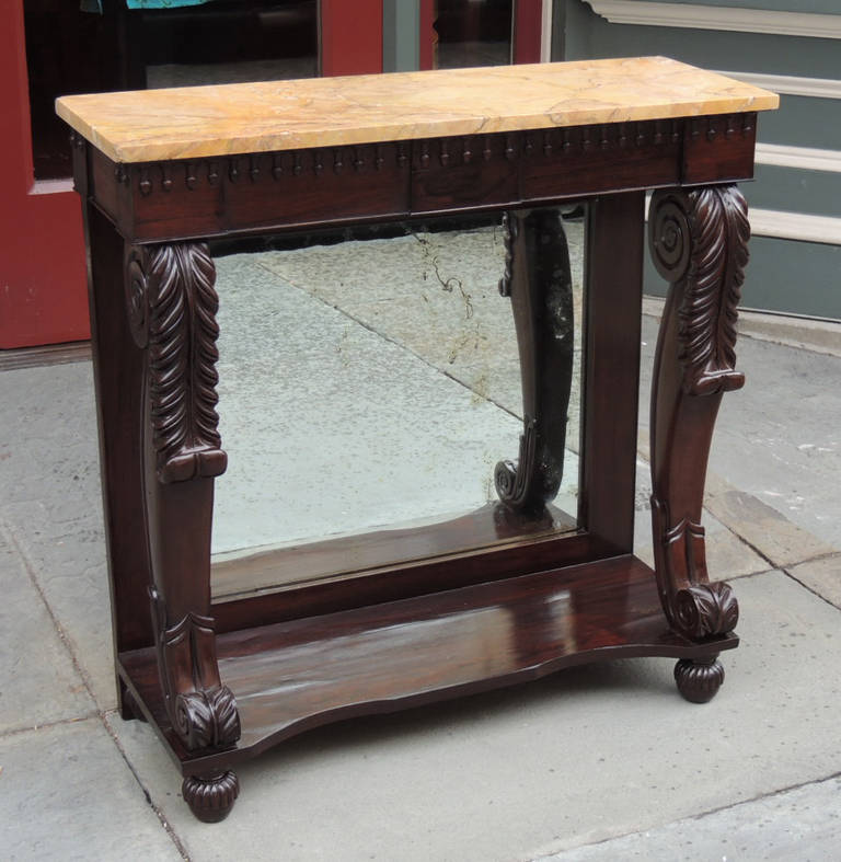 This pier table was made in Boston in the 19th century, circa 1810. It is made of solid rosewood and features beautiful carving all along the sides, bottom, and top. There is a mirror in the center and a marble surface.