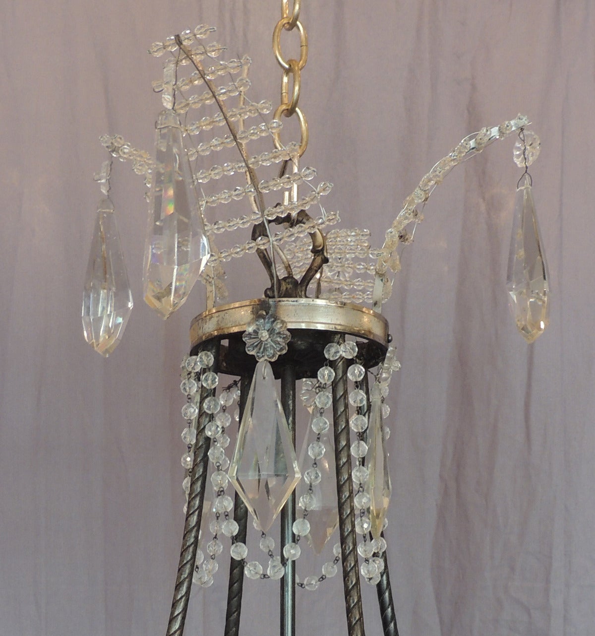 This chandelier was made in Baltic region of Europe in the early-20th century and was made to reflect the Russian Empire style. The chandelier features four crystal fern leaves at the top canopy each with crystal prisms. The stem piece is decorated