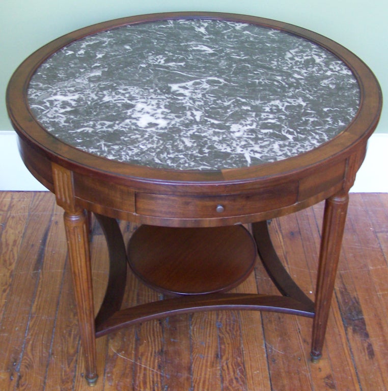 A 19th century French Directoire-style carved mahogany bouillotte table. The apron is fitted with two drawers and two candle slides. The four legs are tapered with fluted sides with circular bronze mounted feet. There is a bottom storage shelf with