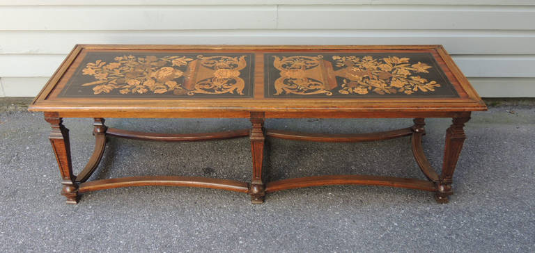 This coffee table was made in Italy and was assembled from parts of varying ages. The top part is older and features marquetry designs on both of the top panels. The design includes pictures of urns, faces and flowers. The base is of newer