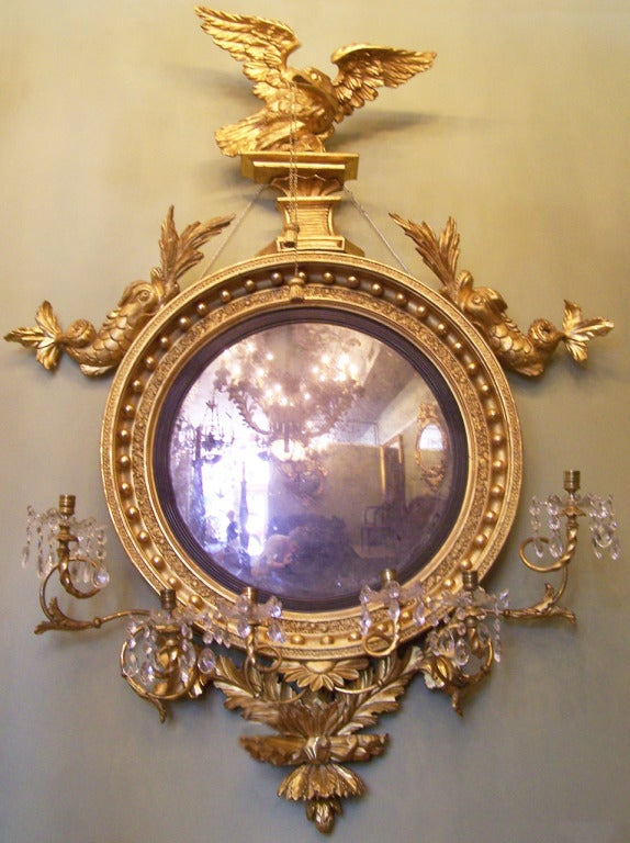 This magnificent English Regency giltwood convex girandole mirror, circa 1800, featuring displayed eagle with hanging tassels, opposing dolphins and six candle arms with gilt foliage and crystal adorned boboches. The original convex mercury mirror