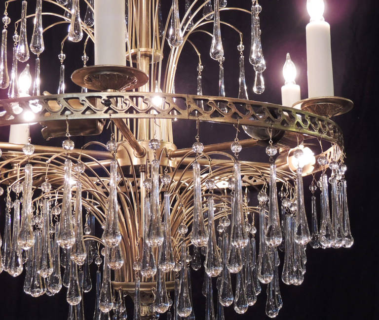 This chandelier was made in Sweden during the mid-20th century and is made of brass and crystal. This piece has a pierced central circular structure with six lights around its perimeter and six lights closer to the chandelier's interior. Small brass