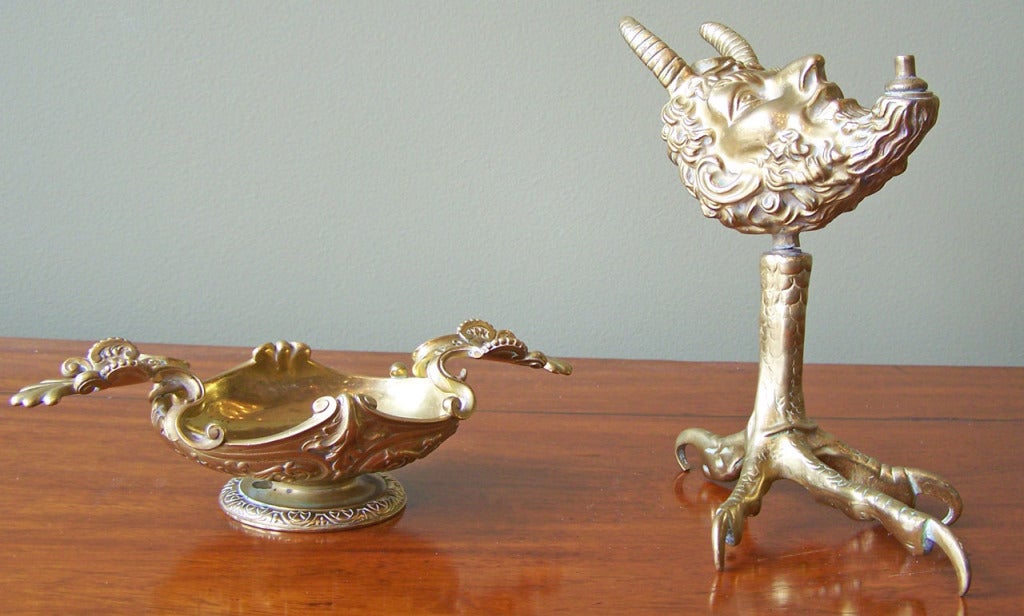 A truly unique cigar lighter, featuring a horned man's head and a rooster's foot. Cigar holder is decorative and scrolled.