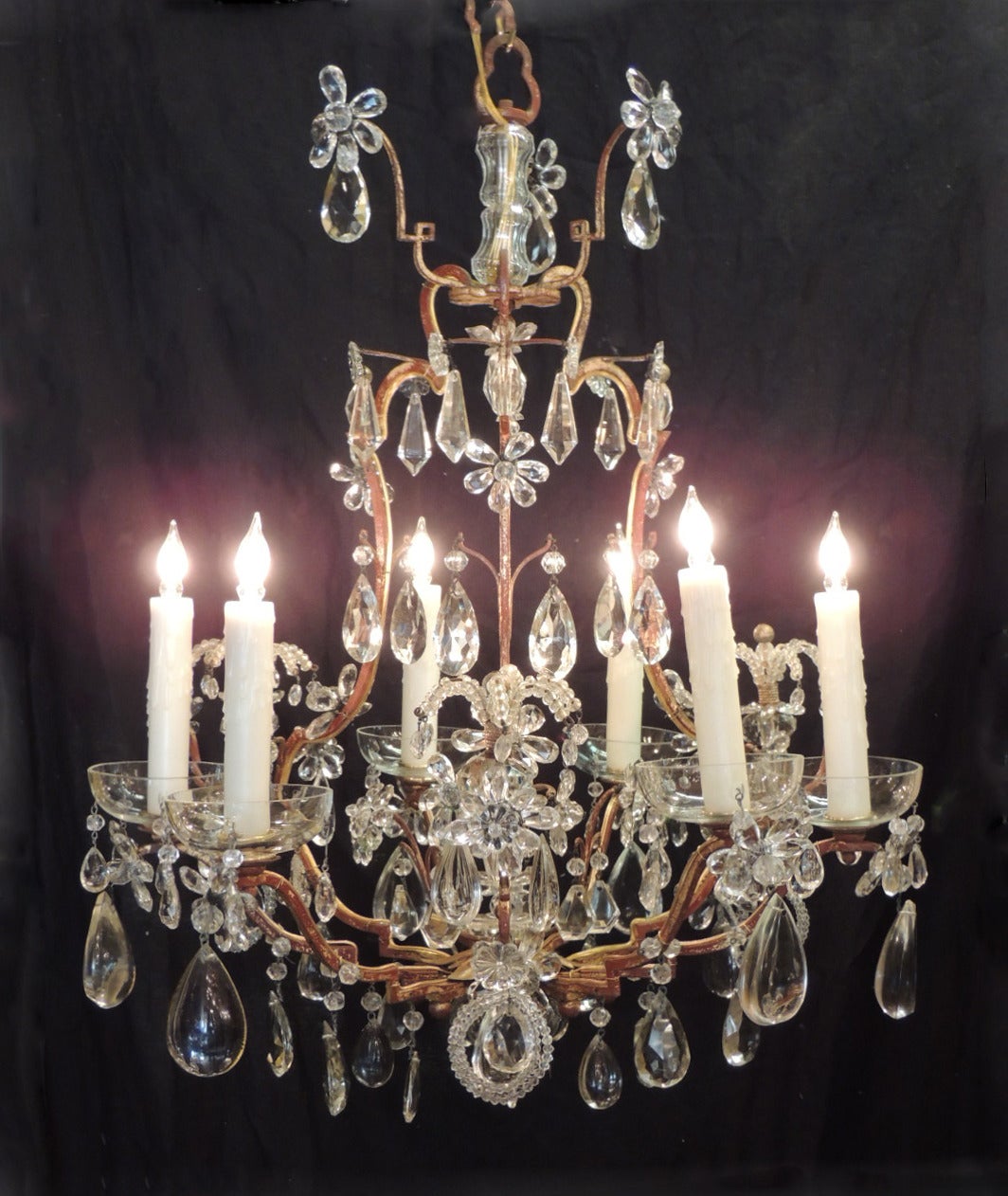 This chandelier was made in France during the first half of the 20th century, circa 1930. It has an iron and tole frame covered in varied shapes and sizes of crystal prisms. The apex of the piece has crystal rosettes and beads. The eight arms are