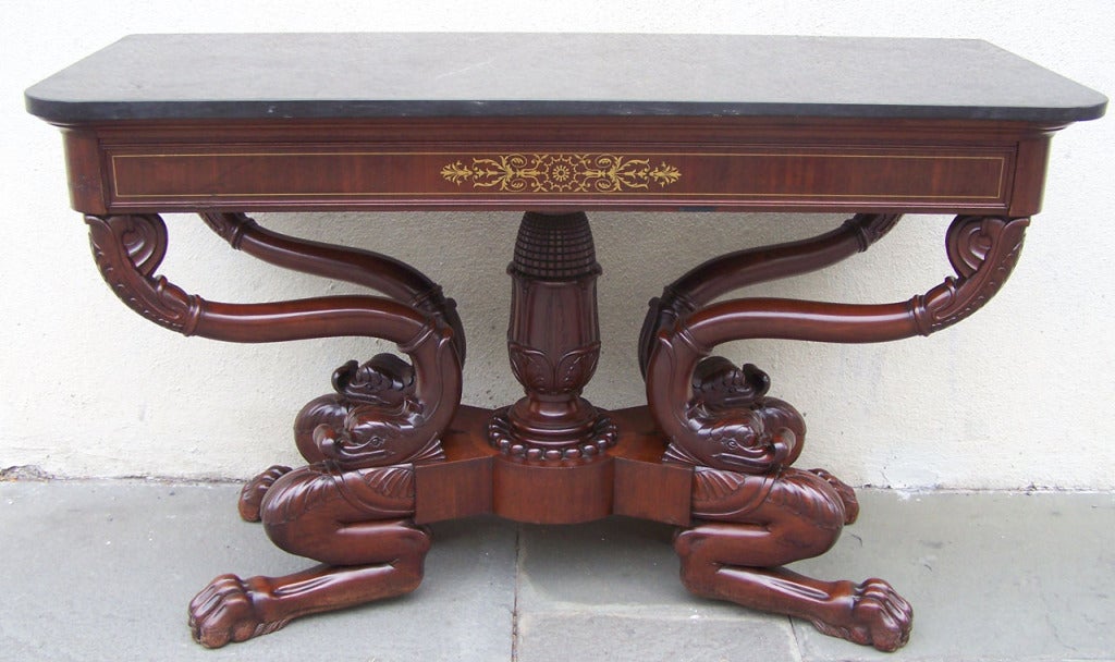 This unusual French mahogany console has elaborate carvings, featuring a center stem with carved maize and four legs with dolphin and and paw feet.  The console has brass inlay and the marble top is original. 

