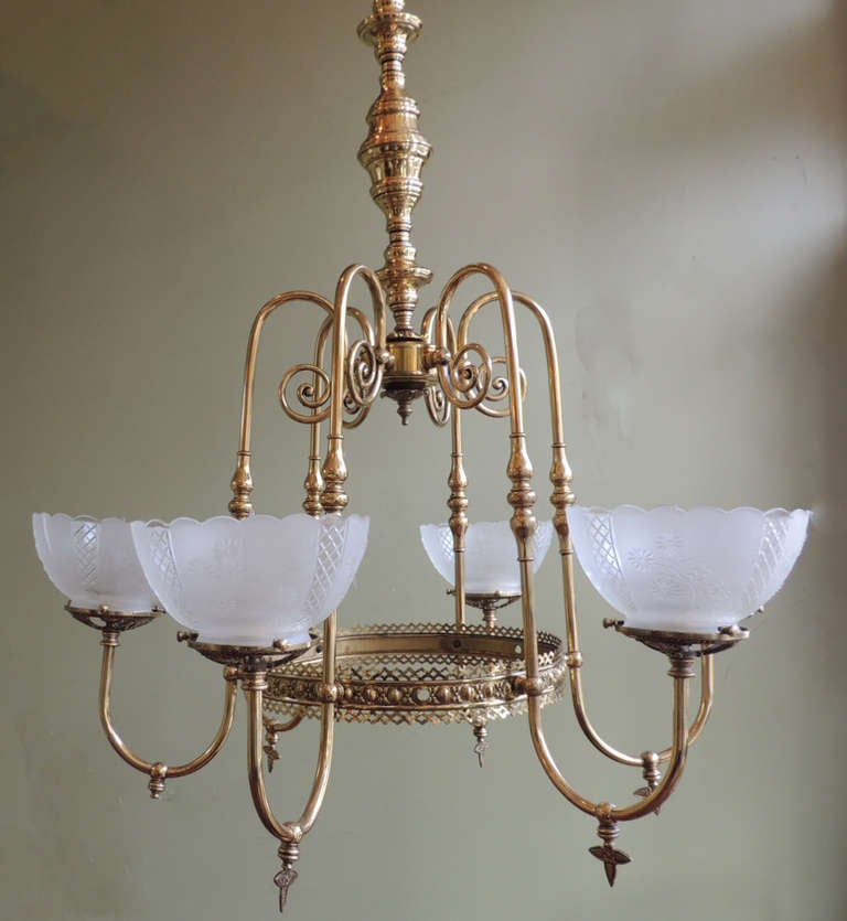 This American brass chandelier was made in the 1870's and was originally lit with gas flame . The brass construction of this piece features scrolls at the top of the chandelier with a decorated circular middle section. The six arms of the chandelier