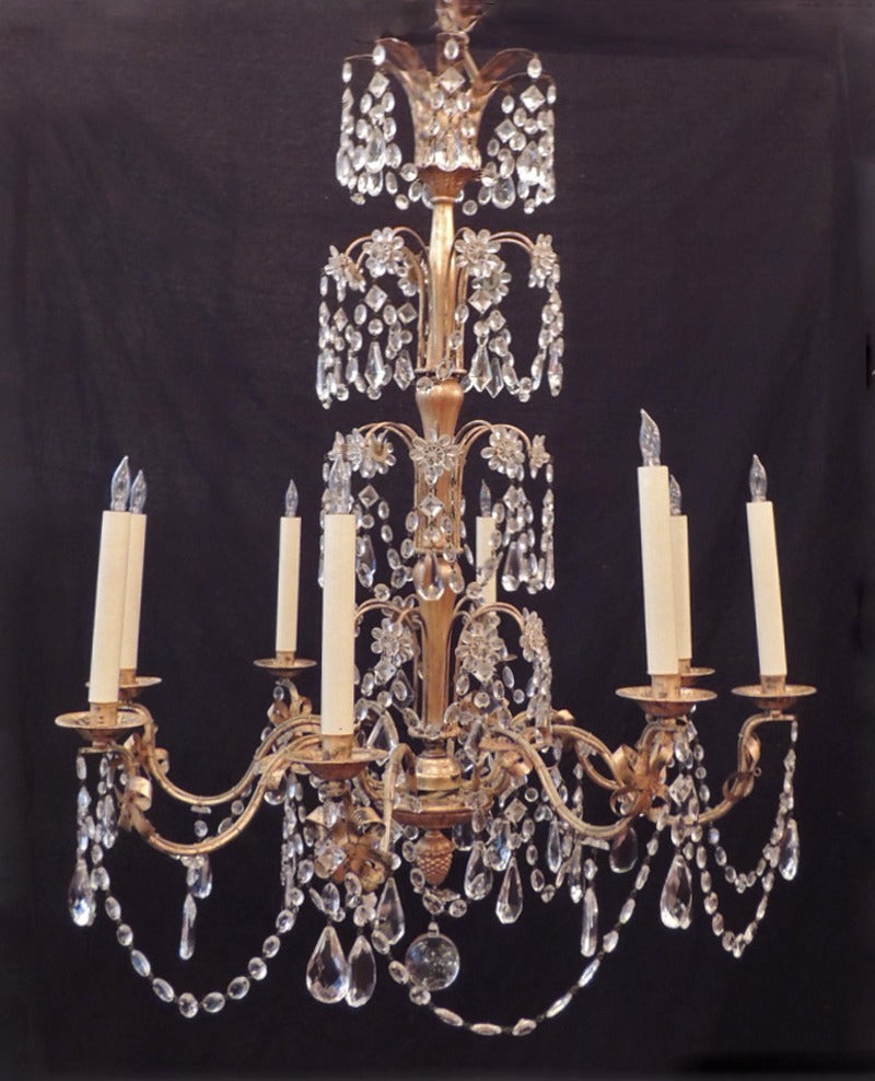 This chandelier was made in France during the mid-20th century, circa 1950. This piece features three tiers of crystal swags, prisms, and rosettes on its upper body. The body is tole with eight candle arms with crystal prisms and swags beneath each