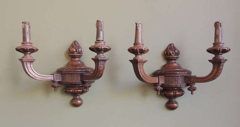 This pair of wooden sconces were made in Italy in the early-20th century, circa 1910. These sconces feature two arms displaying intricate carvings, while the  bodies of the sconces are circular with finial details on the top and bottom.