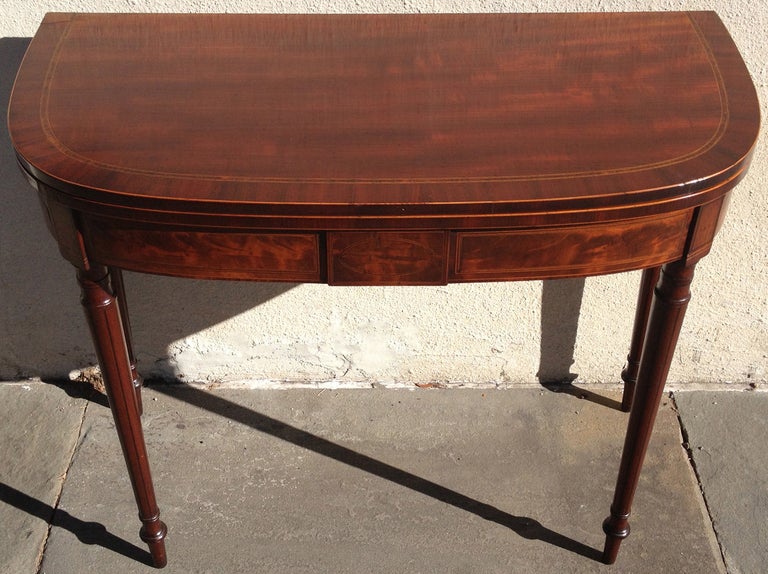 This is an 1800's Boston card table with a book-matched top, revealing a mahogany top when open. This piece features flame mahogany with ebony string inlay and satinwood.