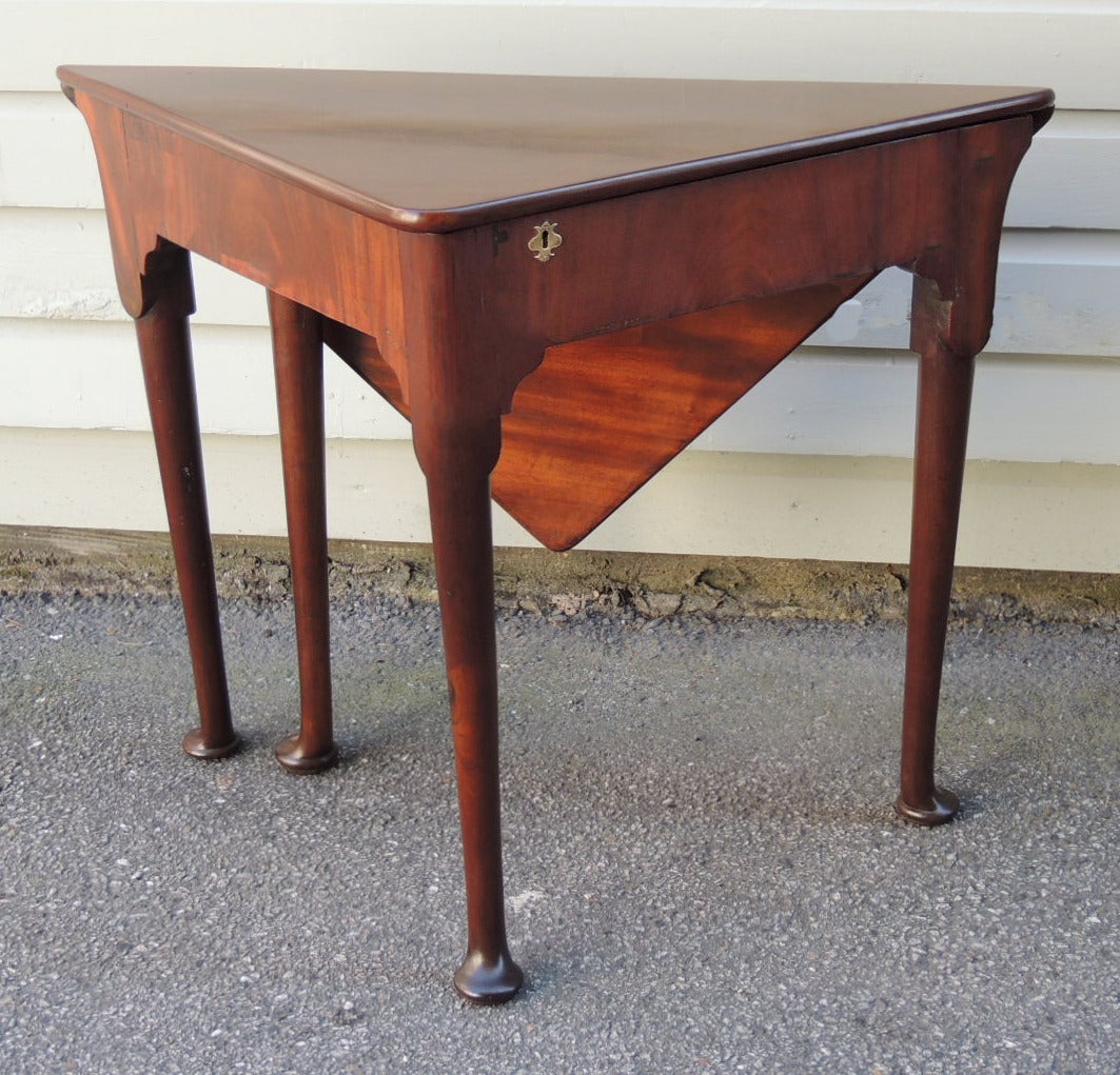 This table was made in England in the first half of the 18th century, circa 1740. This table has a rear drop-leaf that doubles the size of the table when folded up. There is a lock on the front apron of the piece that opens the top of the table for