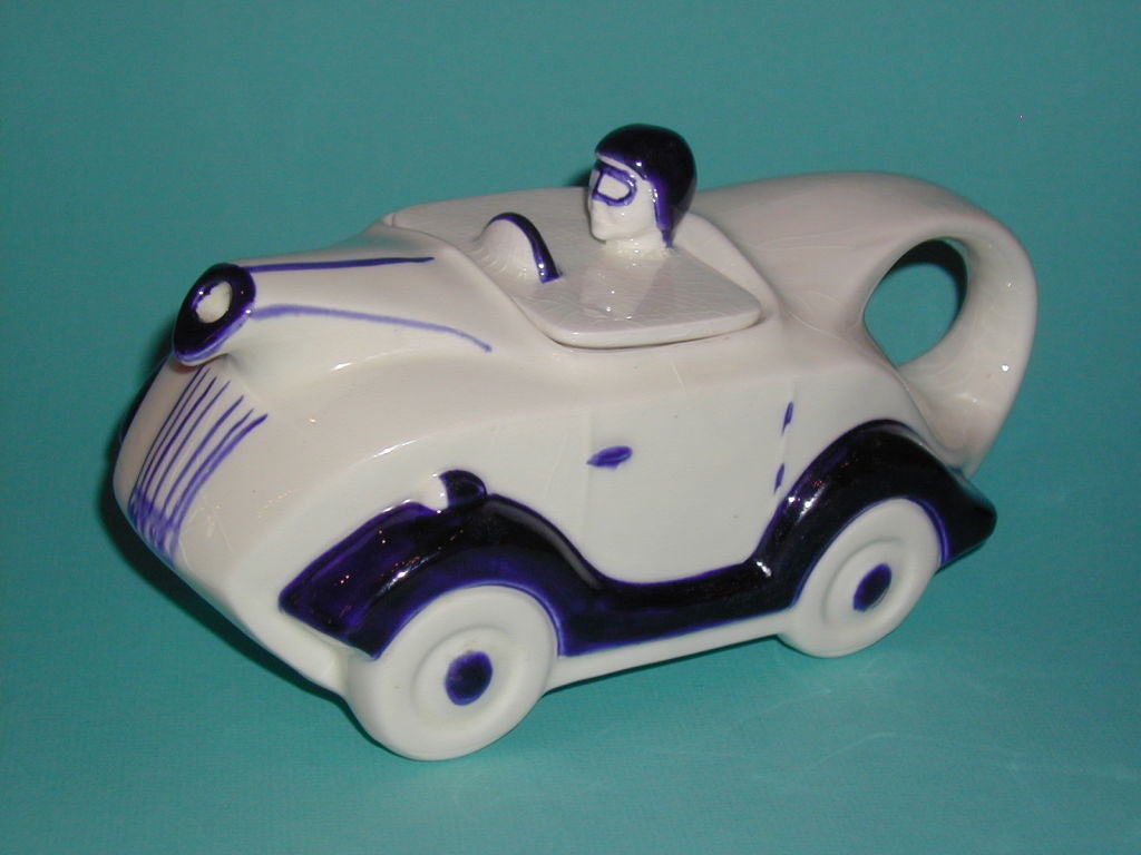 White Glazed Ceramic Racing Car Teapot with Driver in Blue Helmet and other Blue Highlights on Car.