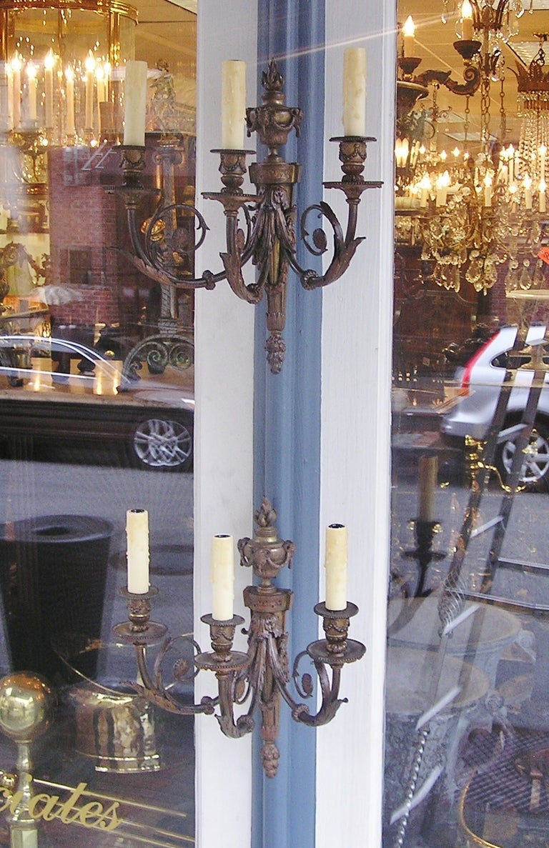 Pair of French bronze three arm sconces with urn top floral swag and rams head finial, scrolled arms, with original bobaches. Originally candle powered.  Dealers please call for trade price.